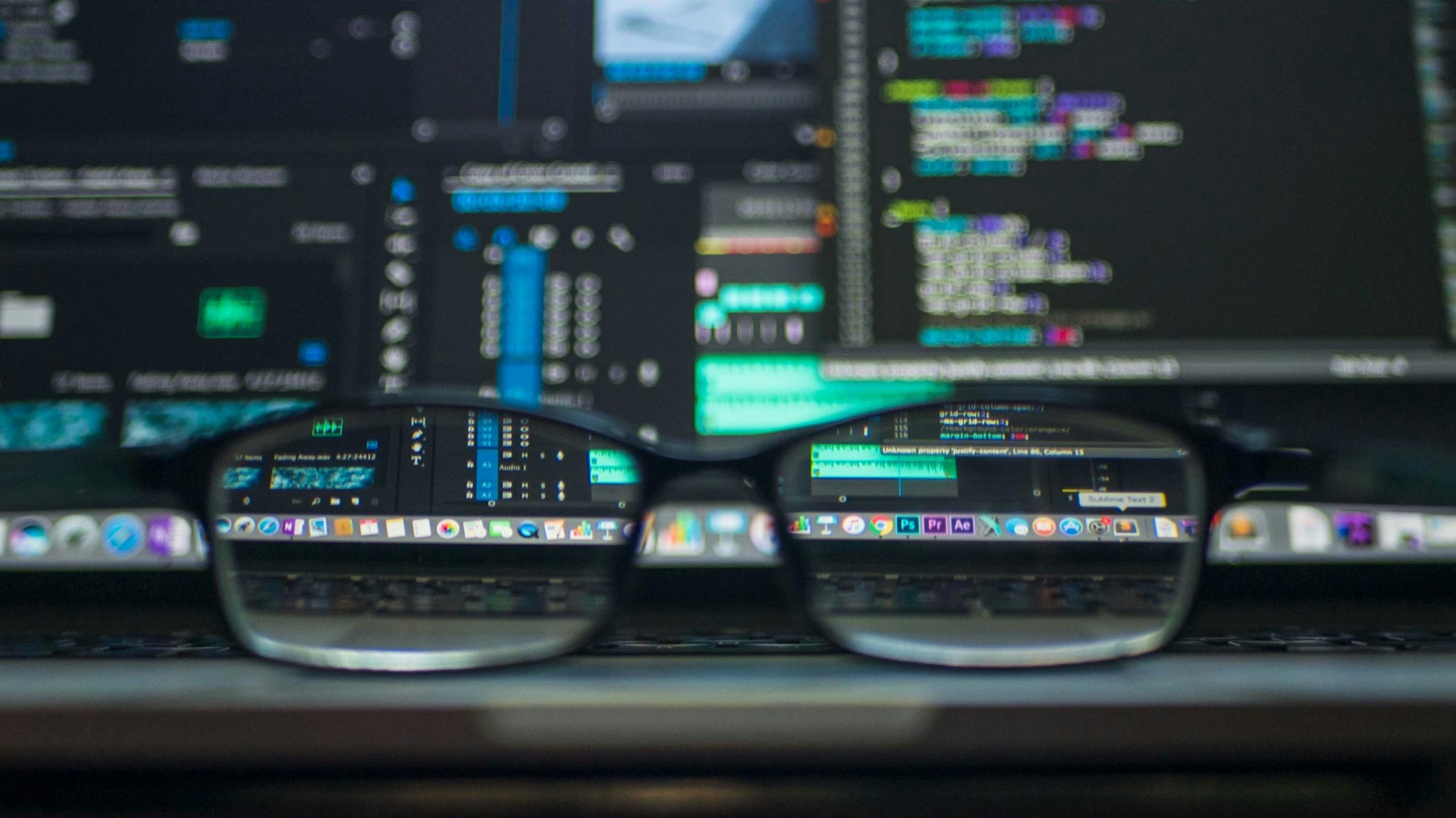 Laptop met een bril op de voorgrond en programmeertaal op de achtergrond (vervaagd)